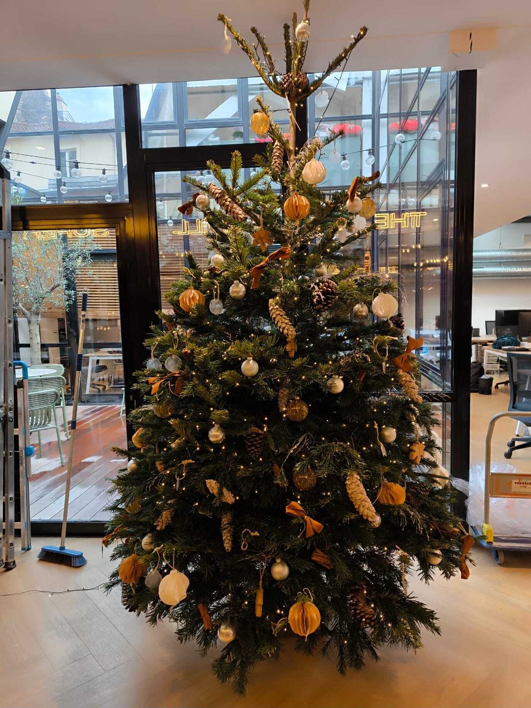 Sapin de Noël naturel décoré en ocre et blanc dans un open space sous verrière